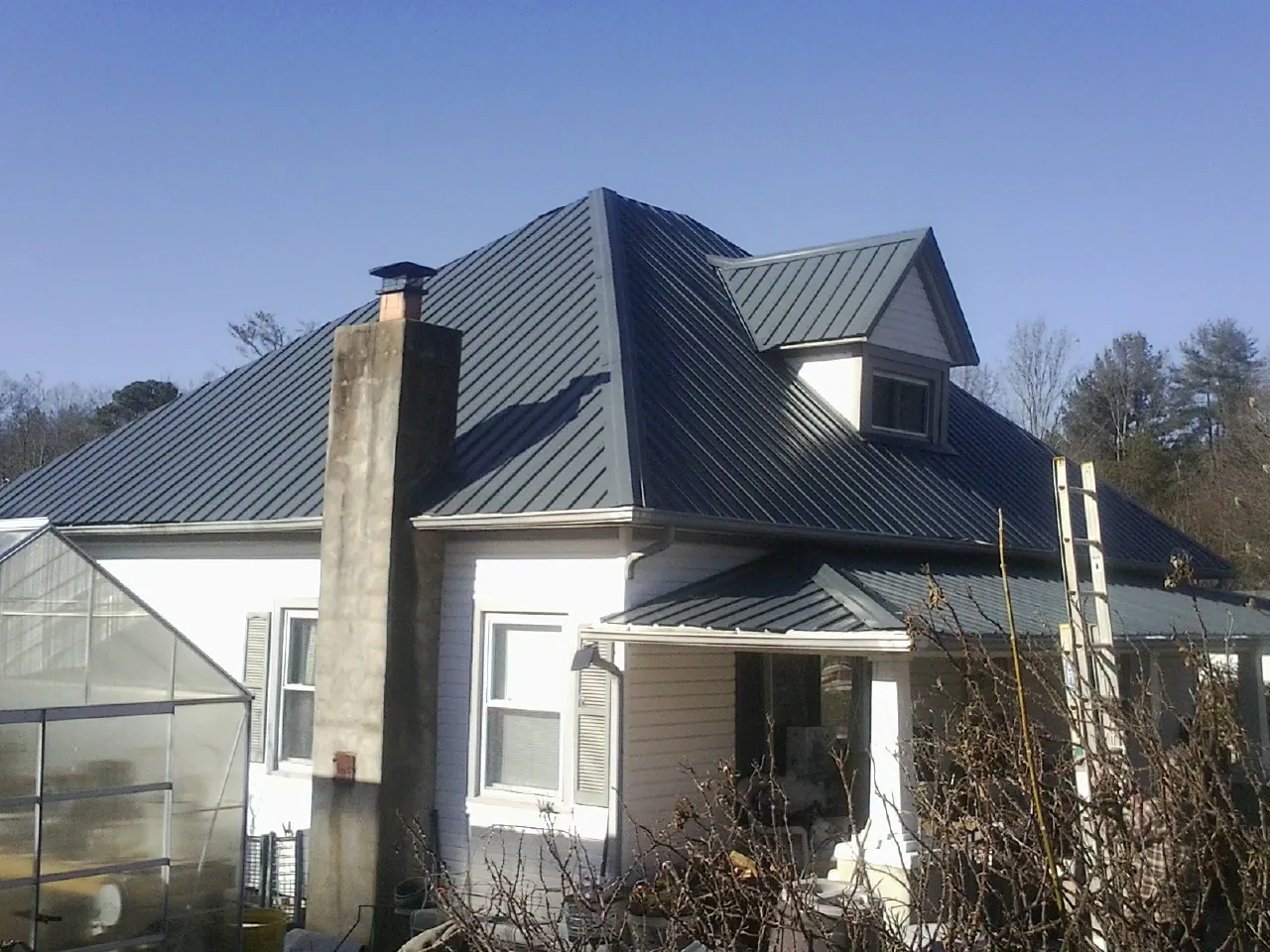 Dark blue standing seam metal roof on a white farmhouse with dormer — Slate & Tile Roof Repair by Roofing Brothers in Minotola