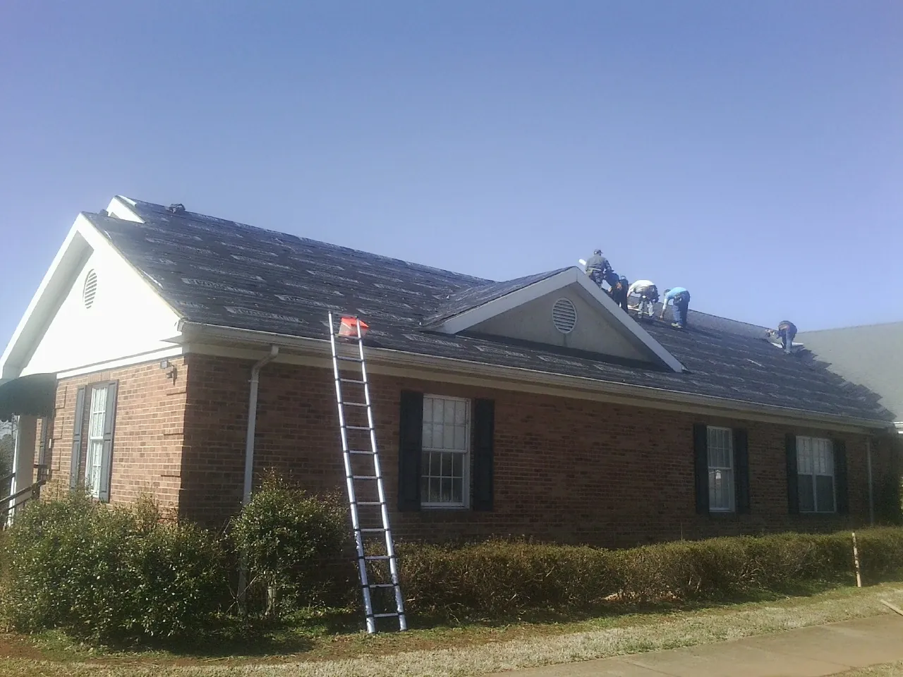 Crew tearing shingles off a brick ranch roof with a ladder set — Metal Roof Repair work by our crew in Minotola