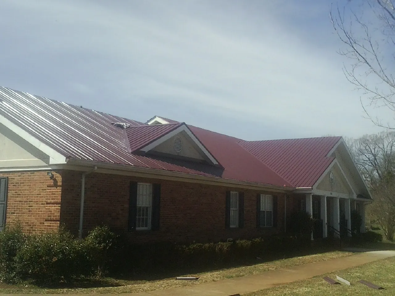 Red metal roof with gabled entries on a long brick building, from a Hail Damage Roof Repair job in Minotola