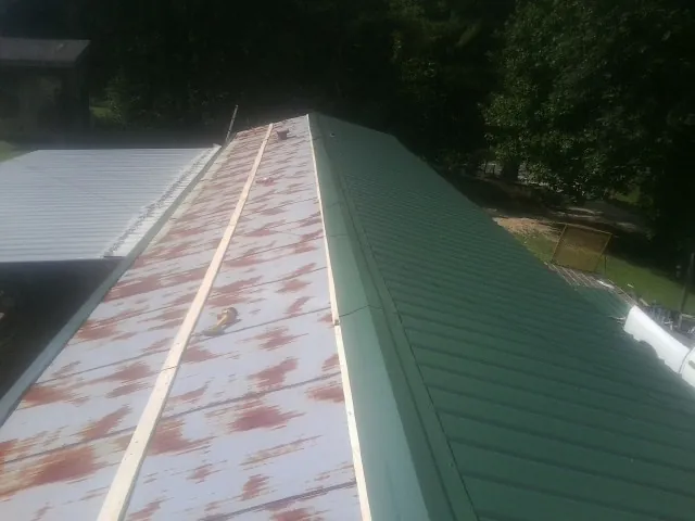 Old rusted panels beside newly installed green metal roofing — Wind Damage Roof Repair by Roofing Brothers in Minotola