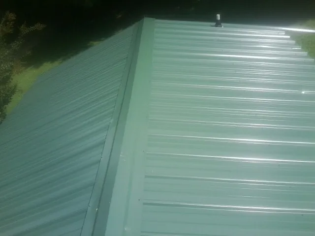 New green metal panels meeting at the ridge of a roof — Flat Roof Repair work by our crew in Minotola