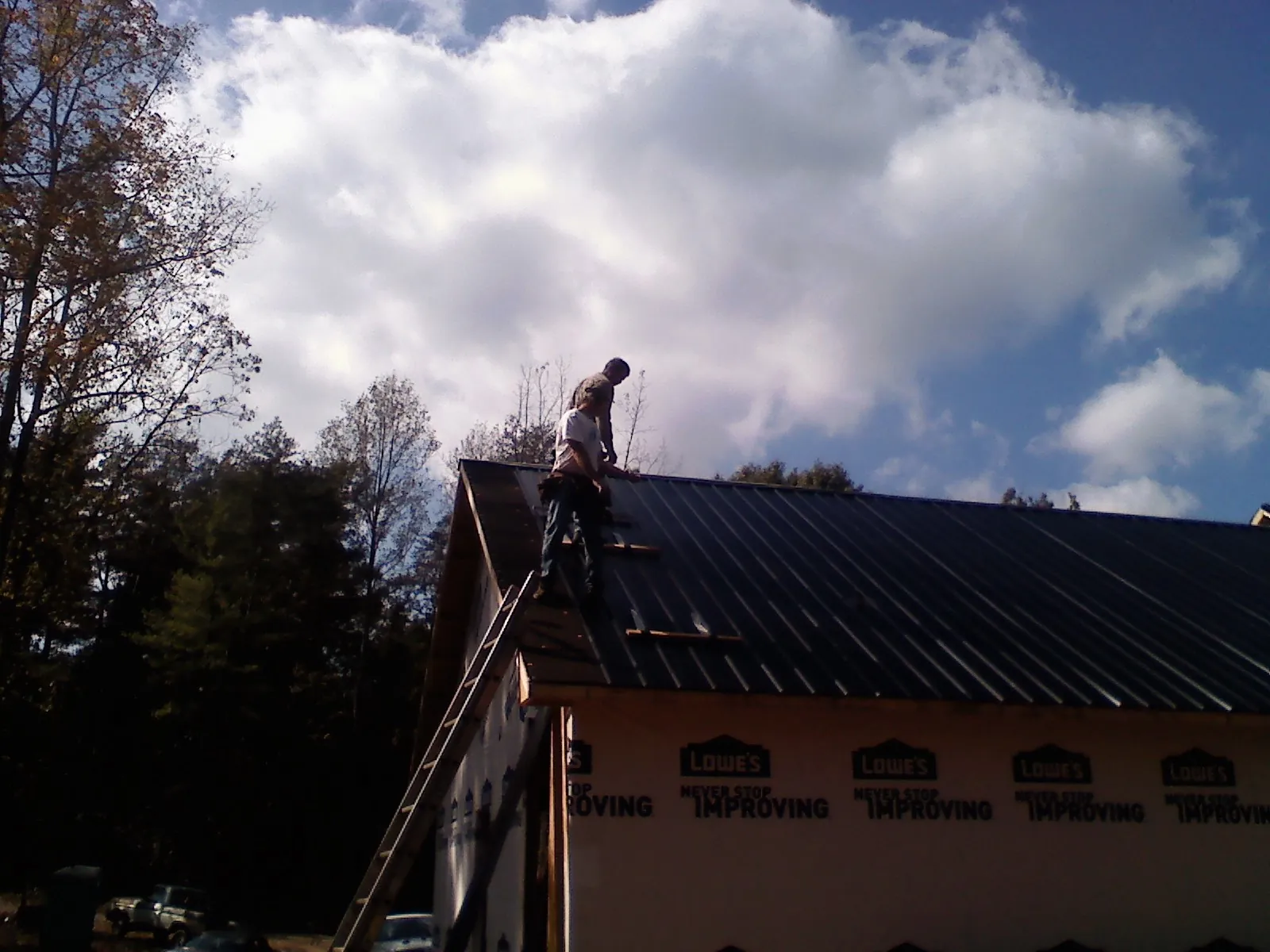 Roofer fastening dark metal panels high against a cloudy sky, from a Roof Inspection job in Minotola