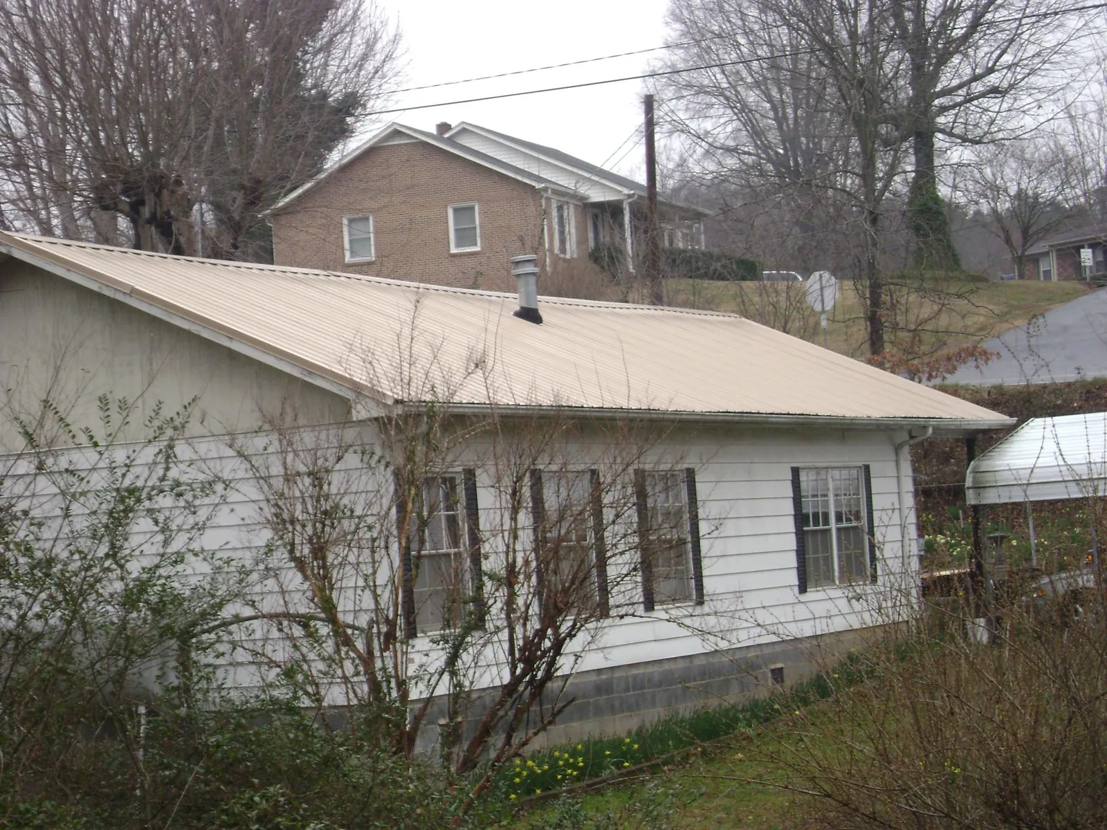 Tan metal roof on a white sided house set into a hillside — Commercial Roofing by Roofing Brothers in Minotola