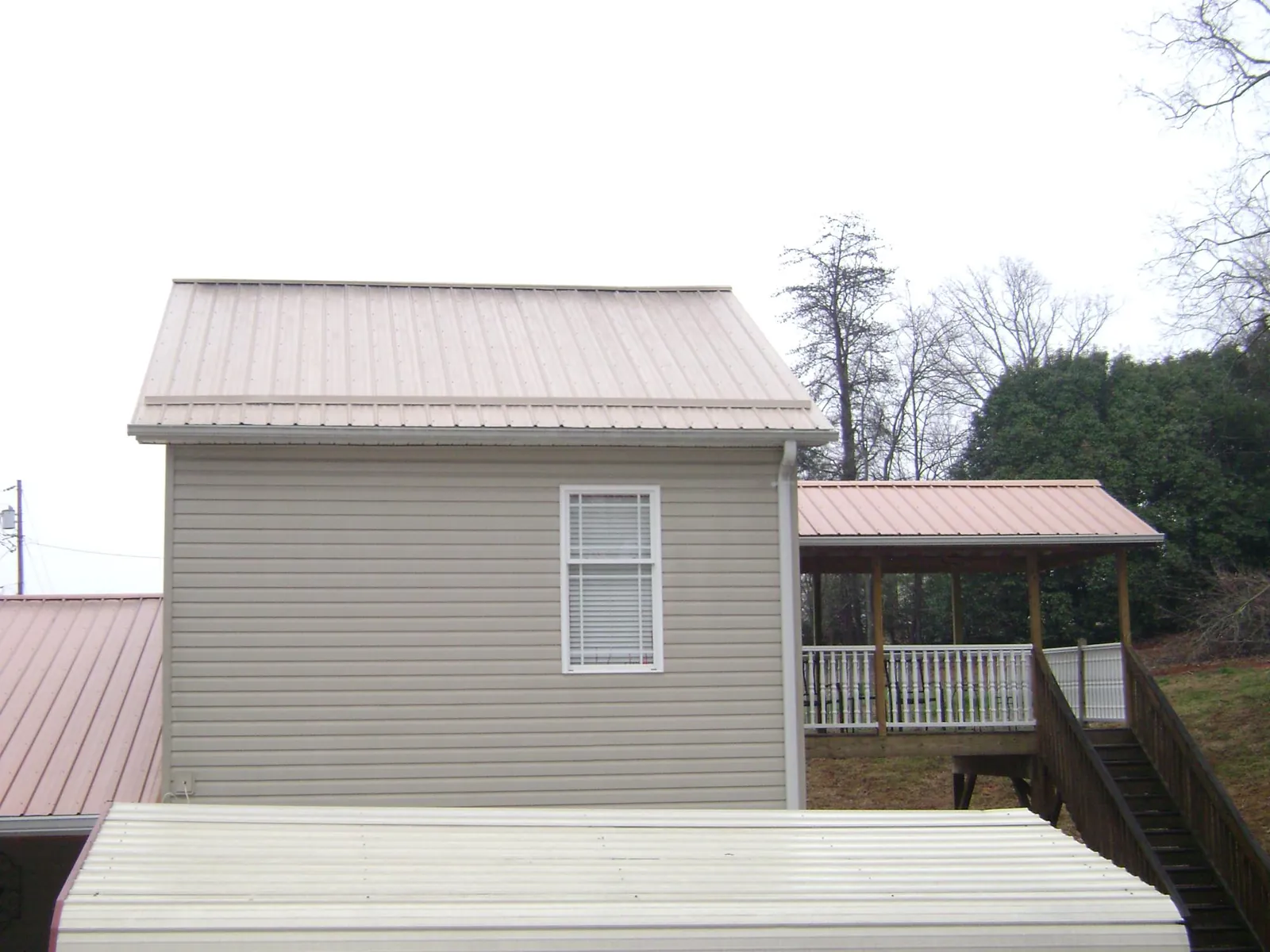 Tan metal roofs on a two story addition and attached porch, from a Roof Replacement job in Minotola